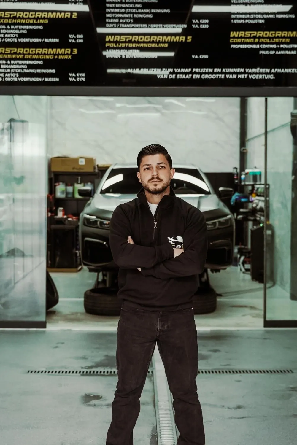 Eigenaar van CarService Brothers voor het prijzenbord in de zaak